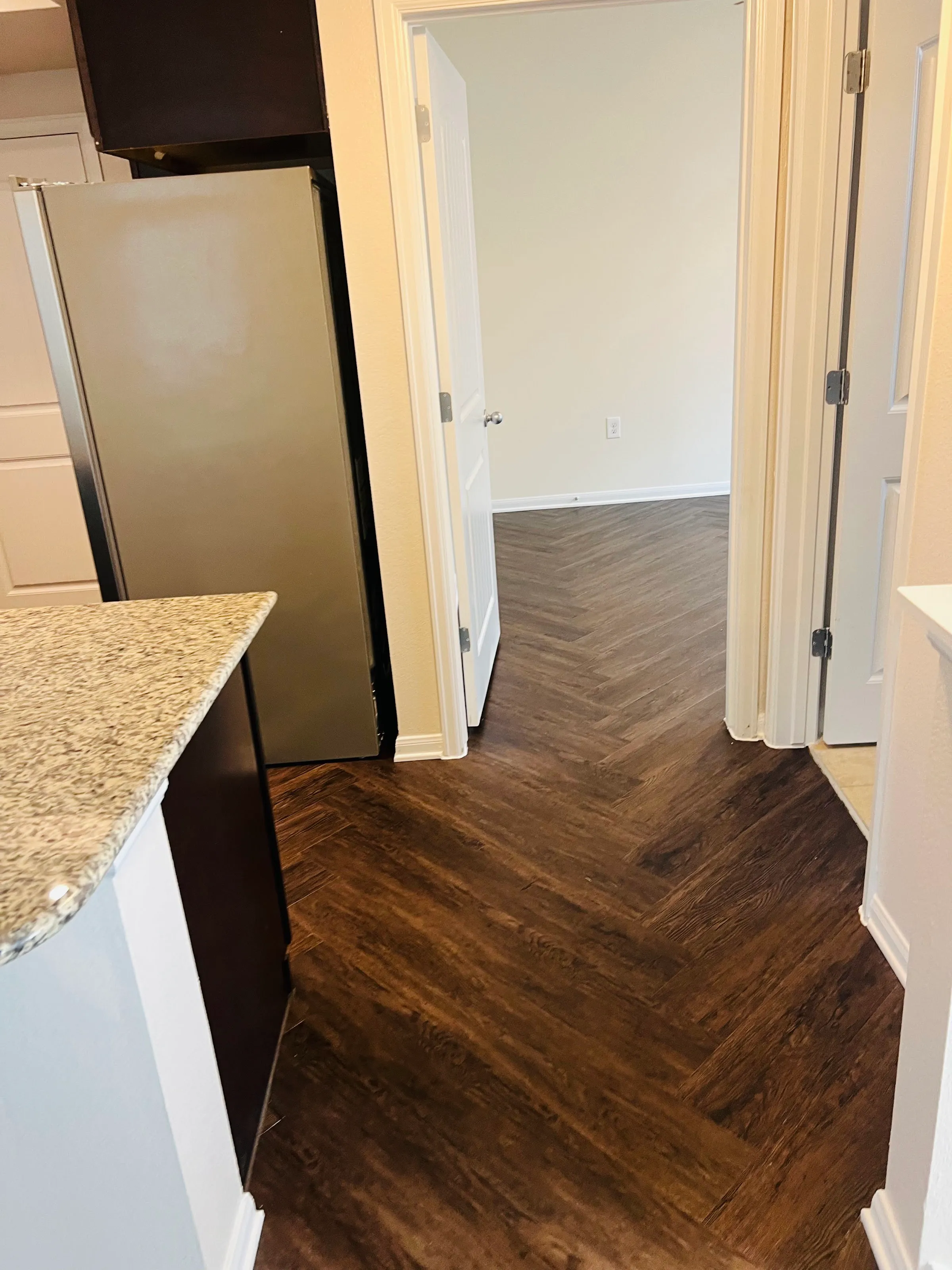 Overhead view of dark LVP herringbone flooring extending from a kitchen area towards a doorway.